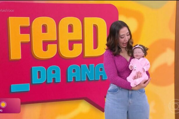 Juju Massaoka segura Bebê Reborn em frente ao telão do Feed da Ana do Mais Você. A repórter olha o bebê com a boca aberta