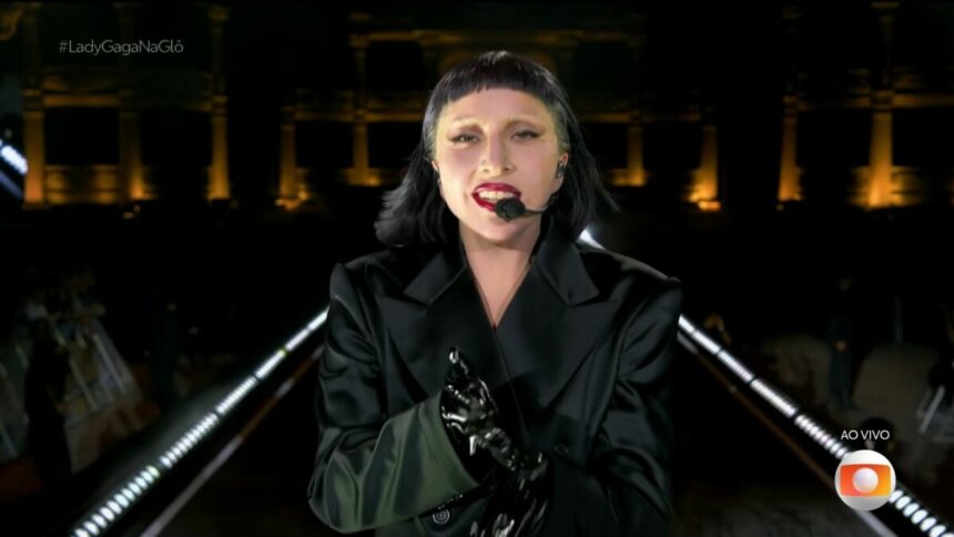 Lady Gaga veste preto, e caminha no palco, no encerramento do show. Ela olha para câmera da transmissão do Globoplay