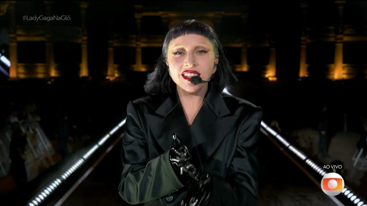 Lady Gaga veste preto, e caminha no palco, no encerramento do show. Ela olha para câmera da transmissão do Globoplay