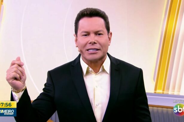 Marcão do povo levanta o braço esquerdo no cenário do Primeiro Impacto no SBT