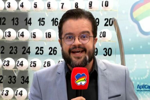 Apresentador do Pernambuco da Sorte em frente ao painel com as bolas do sorteio de 11 de maio. Ele segura um microfone vermelho