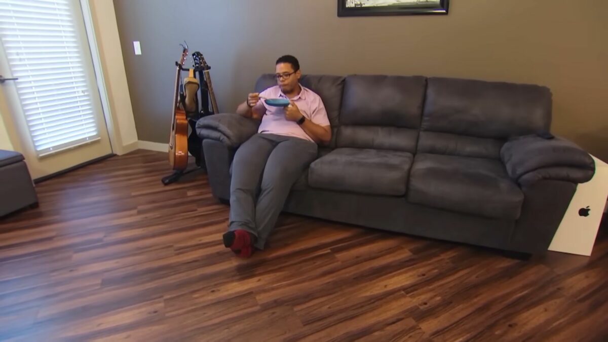 Participante do Quilos Mortais se alimentando, sentado em um sofá, após deixar de ser obeso