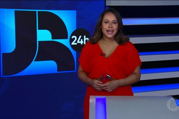 Salcy Lima de vestido vermelho apresentando o Jornal da Record. Ela está em frente ao telão vertical com o logo do JR 24h