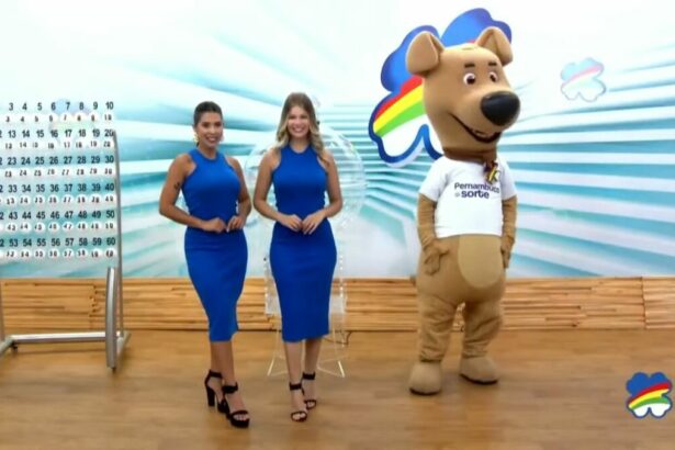 Assistentes de palco vestem azul, posicionadas ao lado do painel com as bolas e o mascote do sorteio do Pernambuco dá Sorte