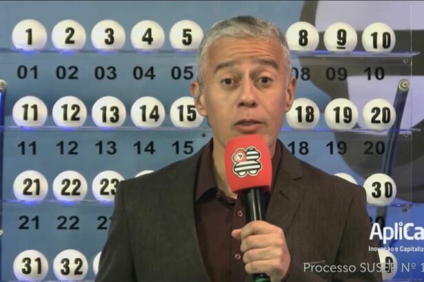 Apresentador do São Paulo da Sorte em frente ao painel com as bolas do sorteio de 11 de maio. Ele segura um microfone vermelho