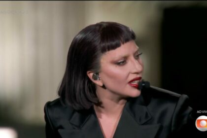 Lady Gaga, veste preto, olha para o lado direito do palco enquanto toca piano em show no Rio de Janeiro