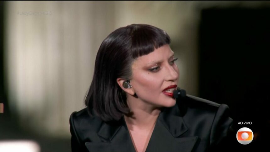 Lady Gaga, veste preto, olha para o lado direito do palco enquanto toca piano em show no Rio de Janeiro