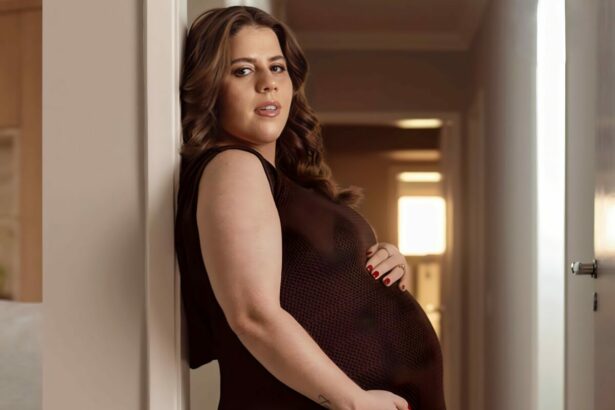 Tati Machado com a mão na barriga ainda grávida. Ela veste um vestido marrom e está encostada em uma parede