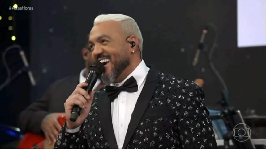 Belo, de terno brilhoso e gravata borboleta, sorrindo no palco do Altas Horas