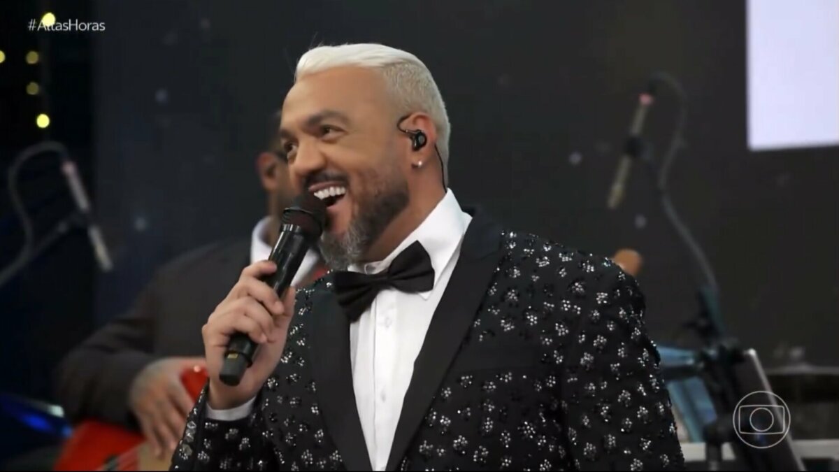 Belo, de terno brilhoso e gravata borboleta, sorrindo no palco do Altas Horas