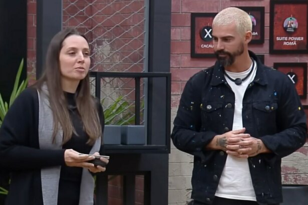 Carol e Radamés em frente ao quadro da divisão de quartos no Power Couple Brasil 7