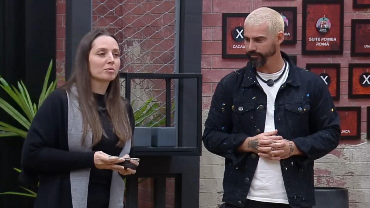 Carol e Radamés em frente ao quadro da divisão de quartos no Power Couple Brasil 7