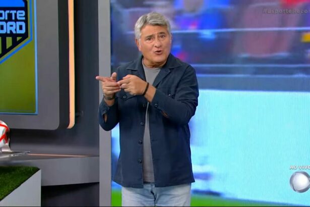 Cleber Machado sorrindo no centro do cenário de transmissão de jogo na RECORD; Narrador está em pé!