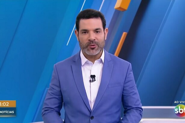 Darlisson Dutra de terno azul e sorridente apresentando o SBT Notícias 1ª edição