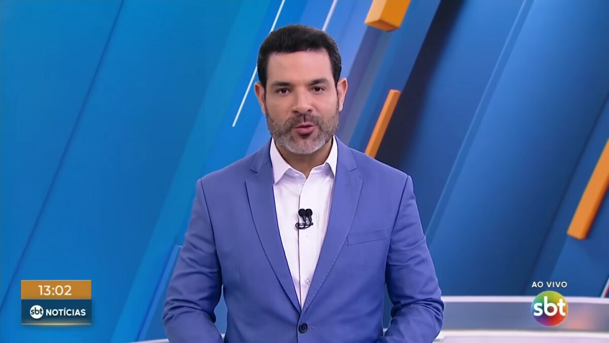 Darlisson Dutra de terno azul e sorridente apresentando o SBT Notícias 1ª edição
