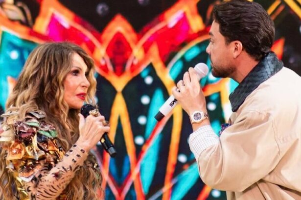 Elba Ramalho e Wesley Safadão cantando enquanto um olha para o outro. Eles usam roupas características de São João