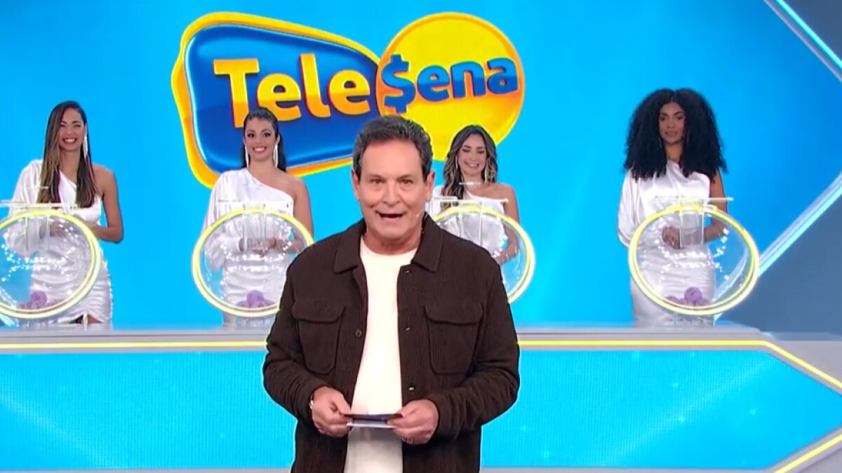 Luis Ricardo caminha no cenário do sorteio da edição 56 da Tele Sena Semanal. O cenário está com artes gráficas azul