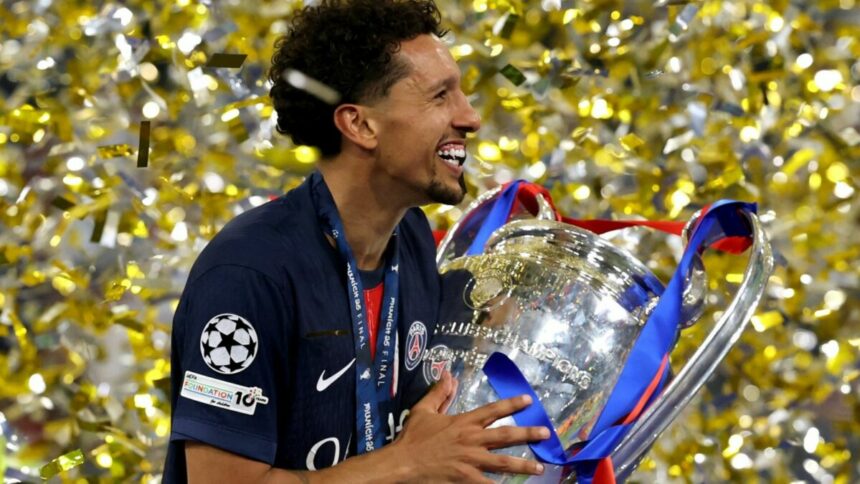 Marquinhos, com a camisa do PSG, segurando a taça da Liga dos Campeões, em meio a chuva de papel picado