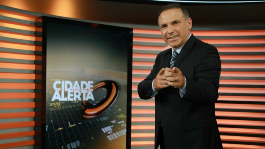 Reinaldo Gottino sorridente, apontando o dedo pra frente, no cenário do Cidade Alerta