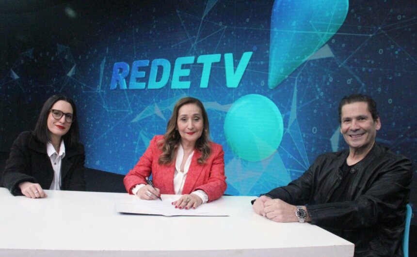 Sônia Abrão no momento em que assina renovação de contrato com a RedeTV! até 2029 com Andrea Dallevo (à esq.) e Elias Abrão (à dir.) por trás dos três o supertelão de LED