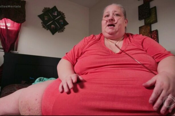 Angela de vestido vermelho, sentada, ocupando todo o sofá por estar muito obesa em cena de Quilos Mortais