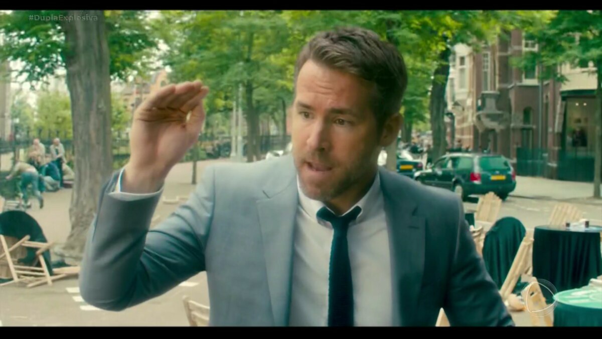 Ryan Reynolds de terno e gravata em cena do filme Dupla Explosiva