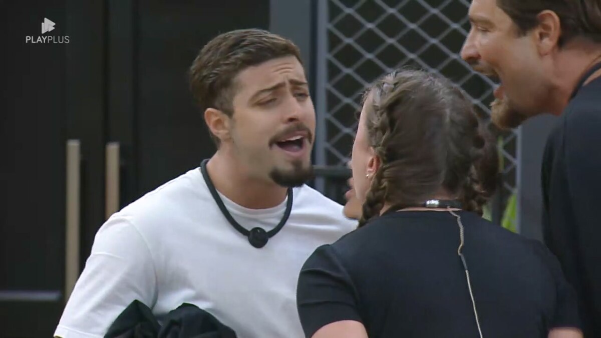 Eike sorrindo debochado cara a cara com Rayanne na sala mansão do Power Couple Brasil 7. Victor e Nat tentam apartar a briga