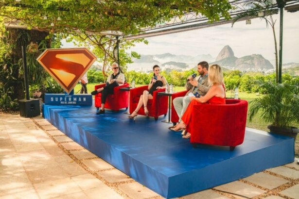 David Corenswet, Rachel Brosnahan e James Gunn sendo entrevistados com o logo do filme Superman ao lado. Ao fundo a paisagem do Rio de Janeiro