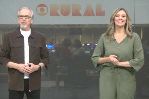 Apresentadores Nélson Araújo e Cristina Vieira em pé no cenário da redação da Globo em São Paulo, ao fundo da redação o logo do Globo Rural no telão