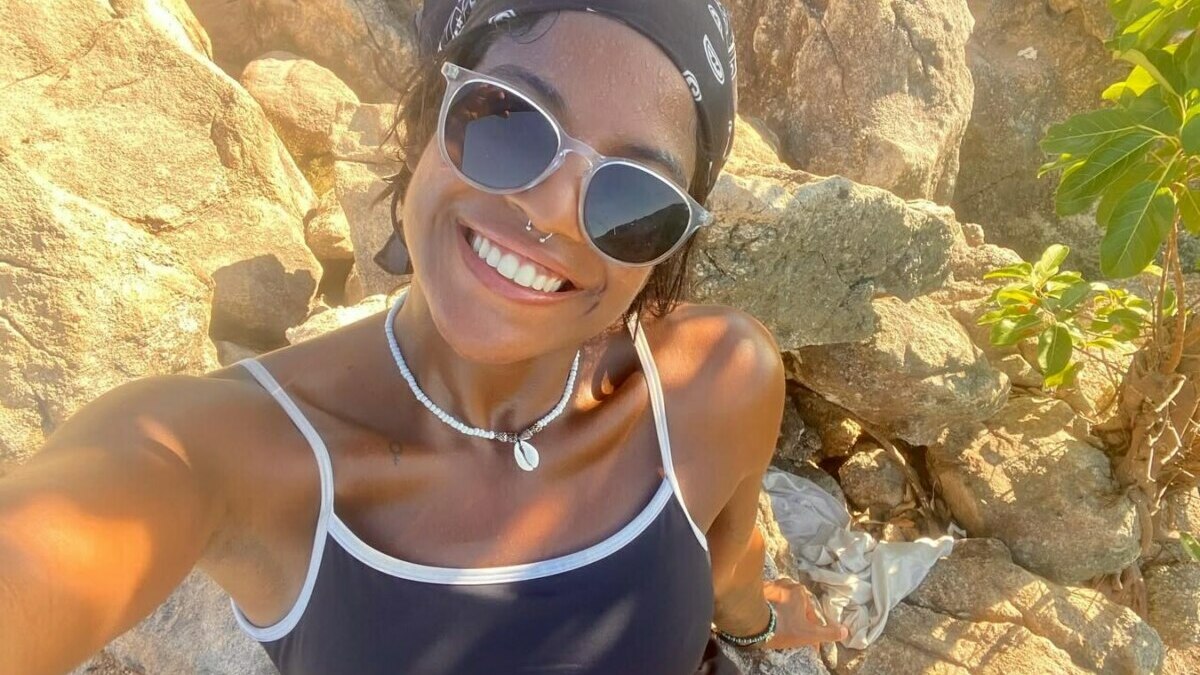 Juliana Marins sorrindo com óculos de sol próximo a umas pedras