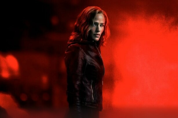 Jennifer Garner com roupa escura em um fundo vermelho escuro na divulgação de A Justiceira