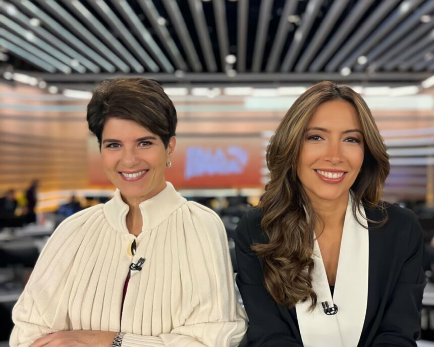 Mariana Godoy e Paloma Poeta sorridentes, em foto posada, na frente da bancada do Fala Brasil