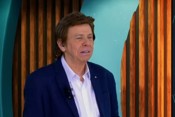 Nelson Rubens de terno e camisa branca no cenário do TV Fama olhando sério para o lado direito