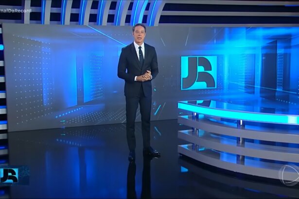 Sergio Aguiar em pé no centro do cenário do jornal da Record vestindo terno preto alguns dias antes de sua demissão. Ele está com semblante sério.