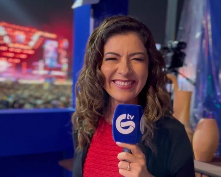 Meiry Lanunce sorrindo e segurando o microfone da TV Guararapes/RECORD. Ao fundo o palco do Pátio do Forró em Caruaru/PE