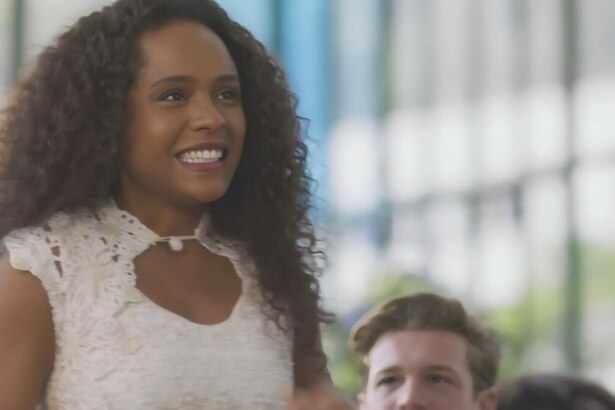 Beatriz (Duda Santos) sorrir ao se levantar para ser homenageada na frente de todos, em cena final de Garota do Momento