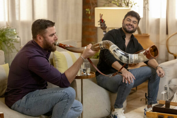 Zé Neto tocando berrante, sentado em um sofá ao lado de Cristiano no 'Viver Sertanejo'