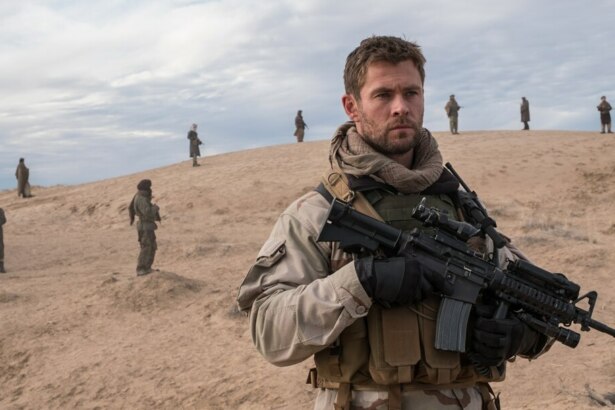 Chris Hemsworth segura arma pesada em um monte. Ele veste roupas de soldado em cena do filme 12 Heróis