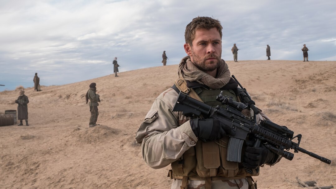 Chris Hemsworth segura arma pesada em um monte. Ele veste roupas de soldado em cena do filme 12 Heróis