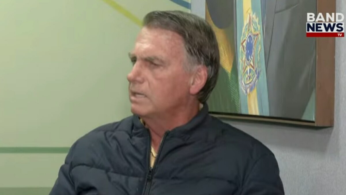 Bolsonaro, vestindo uma jaqueta preta, em tom sério, na entrevista a BandNews TV