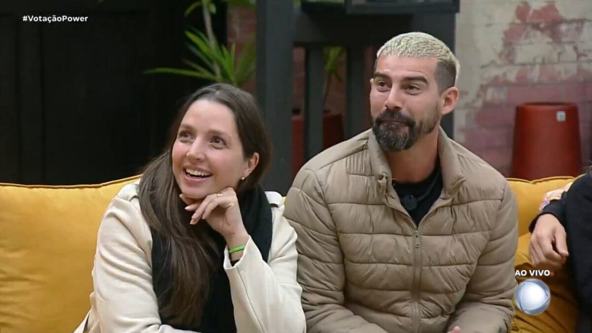 Carol e Radamés sentados no sofá ao acompanhar o resultado da Prova dos Casais no Power Couple