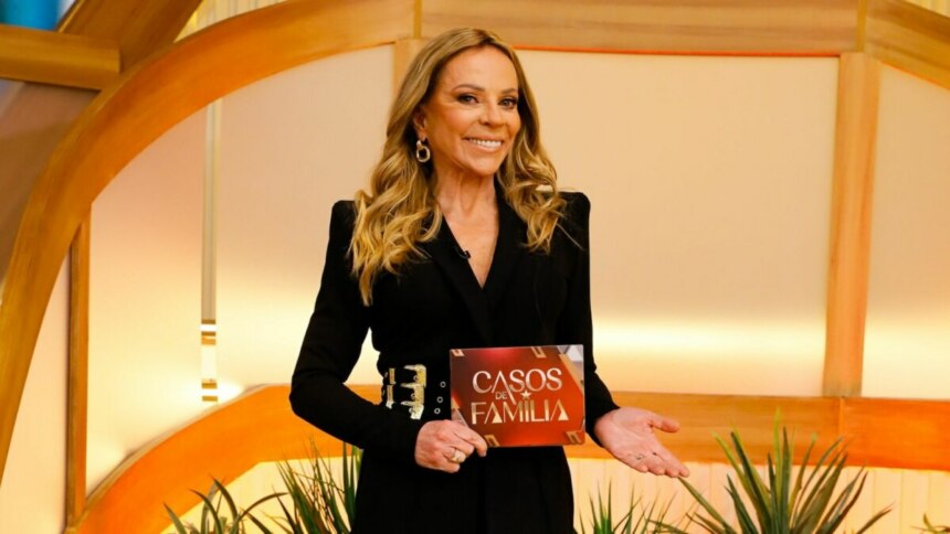 Christina Rocha sorridente, com a ficha do Casos de Família na mão, em foto posada no cenário da nova temporada do programa