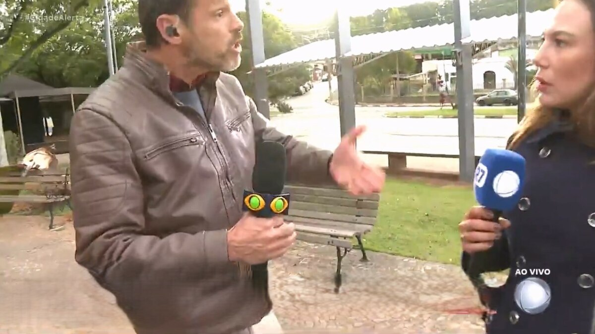 Lucas Martins com o microfone da Band nas mãos gritando com a repórter Grace Abdou que segura o microfone da RECORD