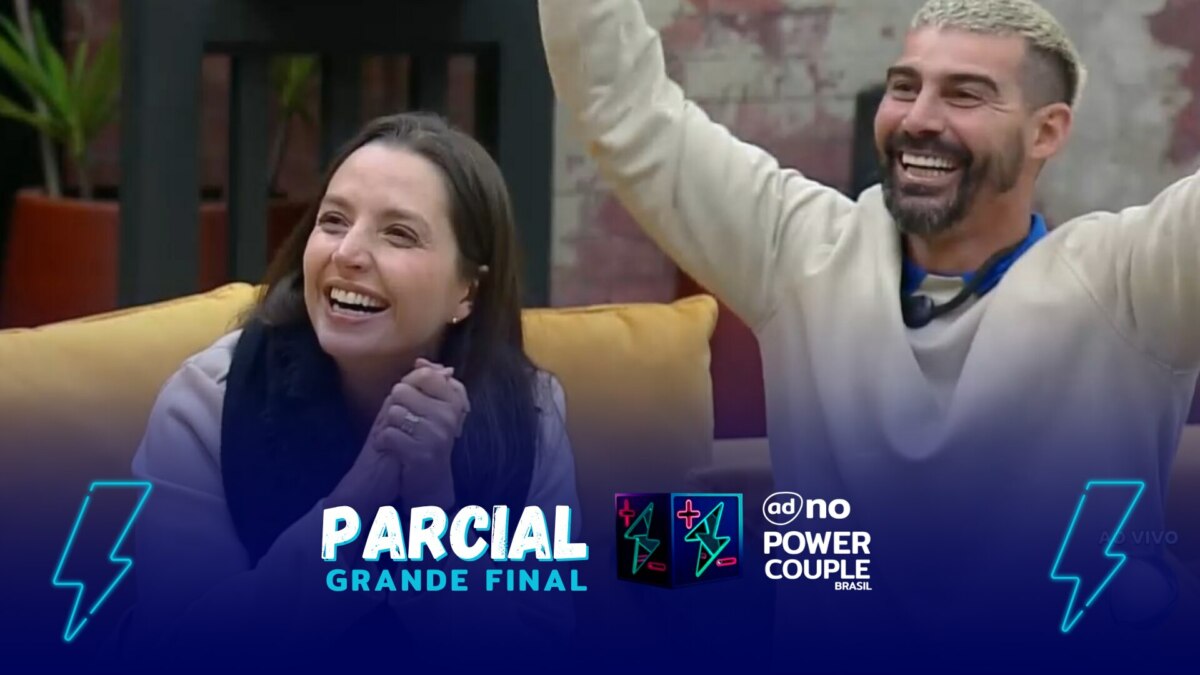 Carol e Radamés comemoram final do Power Couple Brasil 7. Ela está comas mãos unidas sentada no sofá ao lado de Radamés com as mãos levantadas