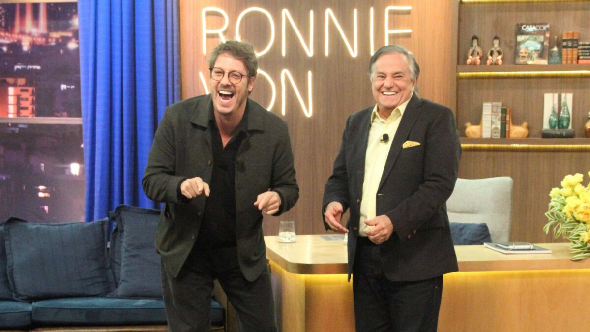 Fábio Porchat e Ronnie Von, sorridentes em frente a bancada, em trecho do Companhia Certa especial de aniversário