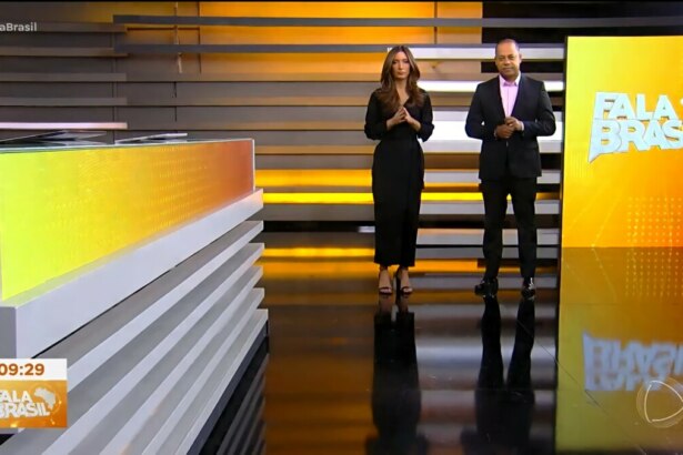 Paloma Poeta e Luiz Fara Monteiro em pé, ao lado do telão do Fala Brasil