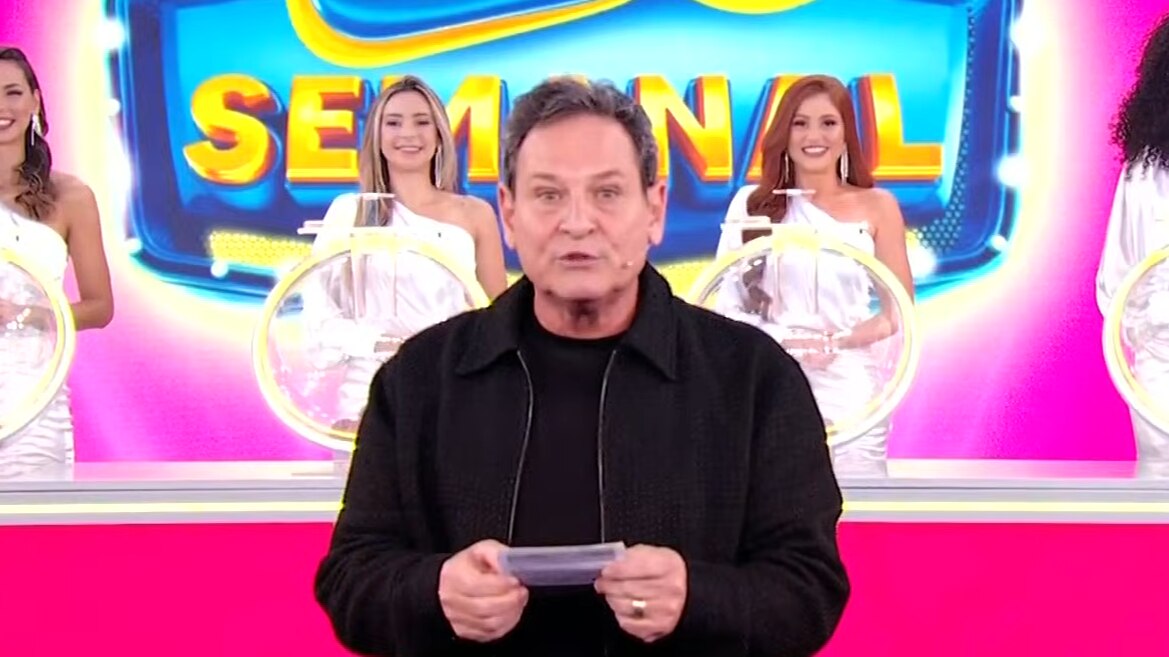 Luis Ricardo segura o bilhete rosa da Tele Sena Semanal edição 60 na frente dos globos e das assistentes de palco