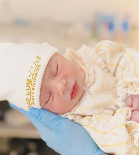 Rosto de Mel. A bebê veste roupa amarela e branco com touca do hospital
