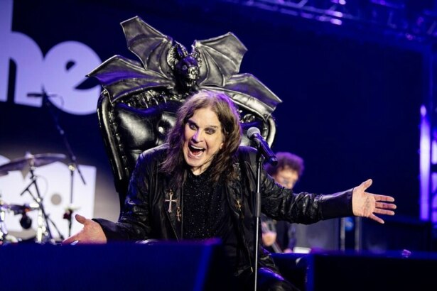 Ozzy Osbourne com a boca aberta e os braços abertos em uma apresentação no palco