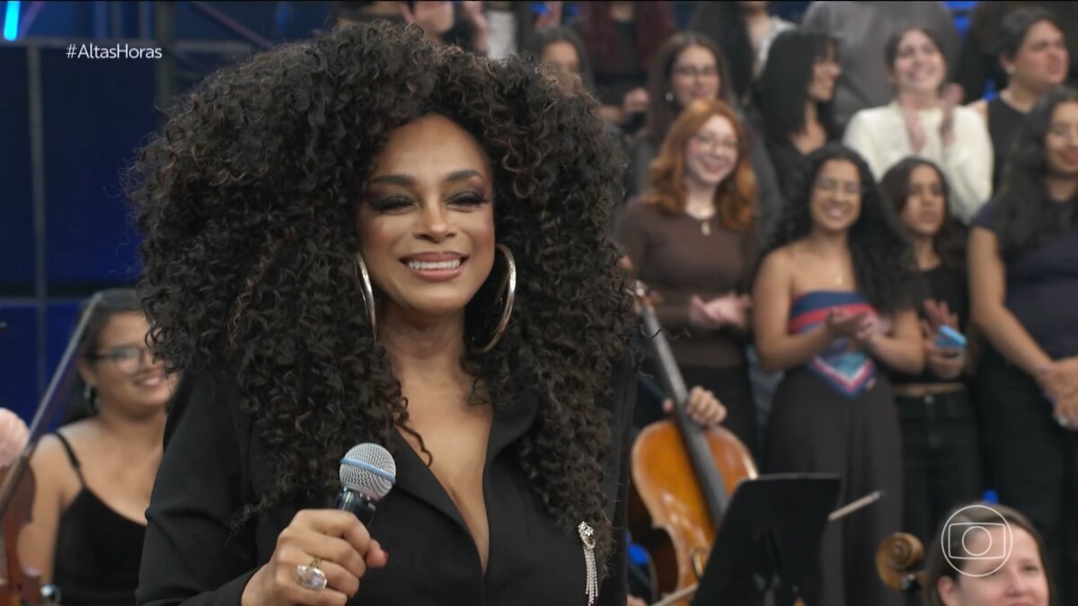 Paula Lima sorrir e segura o microfone no palco do altas Horas